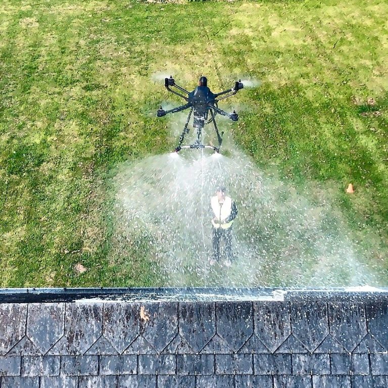 Drone HYDRO-NE pulvérisant de l'eau chaude au-dessus d'une toiture en ardoises, télépilote au sol